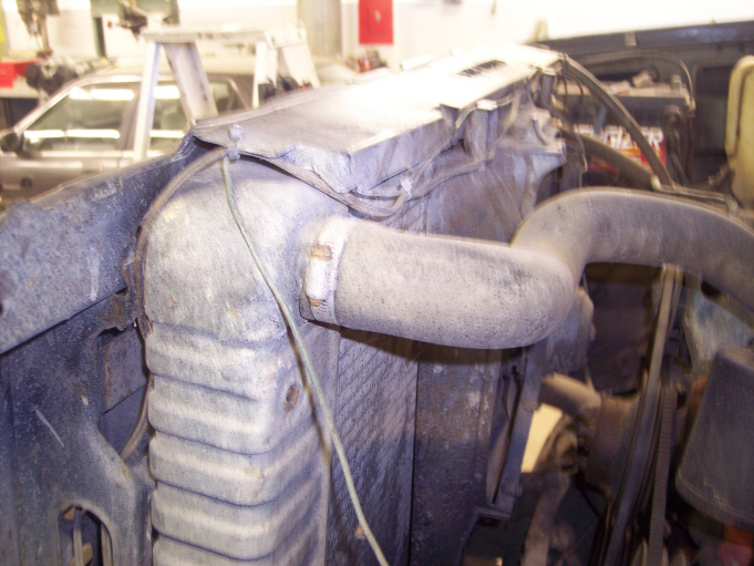 Truck front end with grille removed, showing radiator and taped-off upper hose in a shop