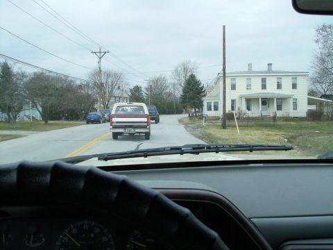 1988 Ford Bronco - A maroon and white Ford F-Series truck drives down a suburban street past houses and trees.