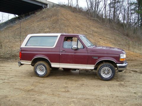 1988 Ford Bronco - This maroon and white Ford Bronco is parked on a dirt road beneath a concrete overpass.
