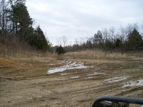 1988 Ford Bronco - A muddy track winds through a field, marked by tire ruts and puddles under an overcast sky.