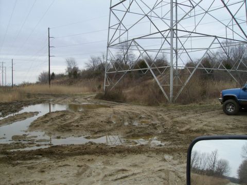 1988 Ford Bronco - Blue pickup truck navigates a muddy off-road path near a power line tower.