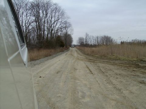 1988 Ford Bronco - Two vehicles travel down a dusty, rural dirt road under an overcast sky.