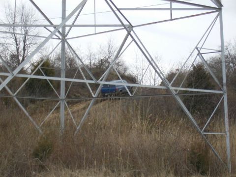 1988 Ford Bronco - A blue SUV navigates a grassy incline near a large metal power line tower.