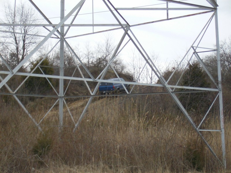 Blue SUV driving on a grassy hill next to a power line tower