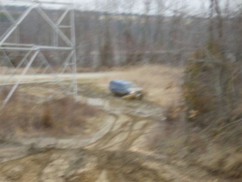 1988 Ford Bronco - A blue SUV navigates a muddy terrain next to a large power line tower.