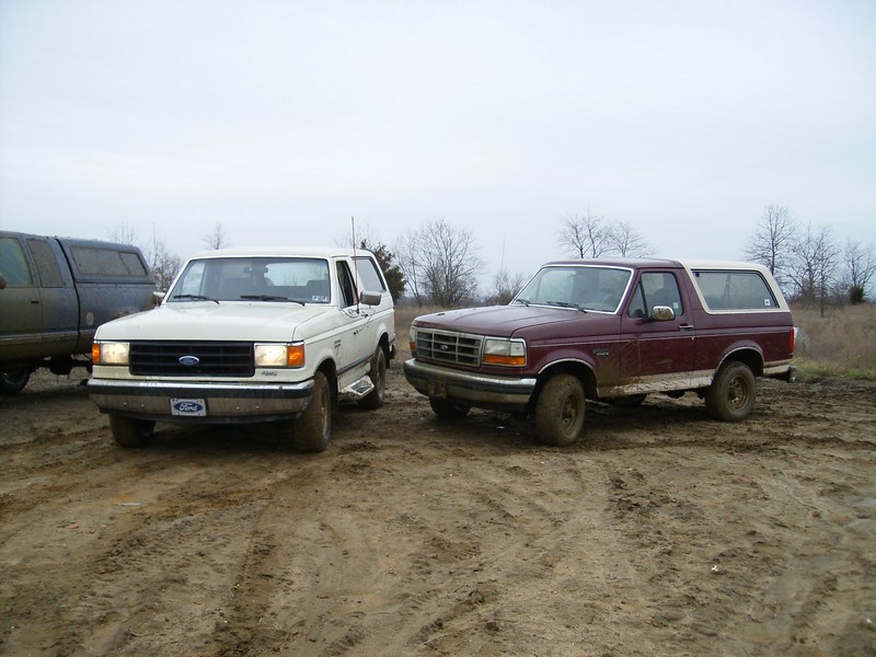 Two Ford Broncos, one white and one maroon, parked on a muddy track