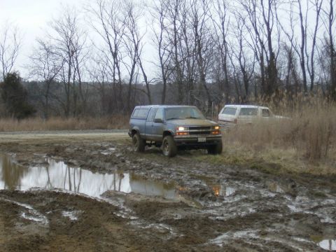 1988 Ford Bronco - Two trucks navigate a challenging muddy terrain under an overcast sky.