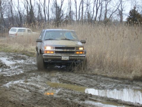 1988 Ford Bronco - A muddy SUV navigates a challenging off-road terrain with another vehicle visible in the background.