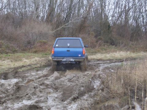 1988 Ford Bronco - A blue pickup truck navigates a challenging muddy off-road course.