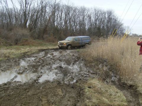 1988 Ford Bronco - A muddy pickup truck navigates a difficult off-road path through a muddy field.