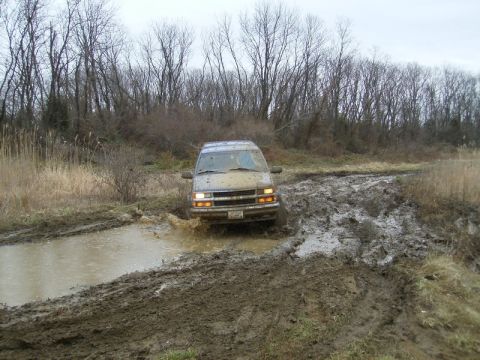 1988 Ford Bronco - This SUV navigates a muddy trail, kicking up water as it goes.