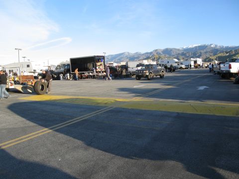 1986 Ford Bronco - Swap meet scene with multiple vehicles and vendors under a clear sky.