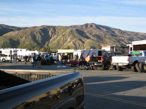 1986 Ford Bronco - A busy swap meet unfolds with vehicles and vendors under a clear sky with mountains in the background.
