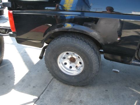 1986 Ford Bronco - The rear quarter panel of a black Ford Bronco shows its large tire and exhaust pipe.
