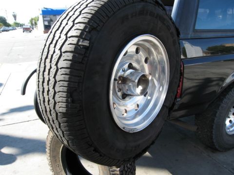 1986 Ford Bronco - A spare tire is mounted on the rear of a black SUV, with the Supermotors.net logo visible.