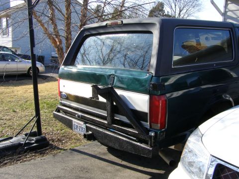 1993 Ford Bronco - Rear view of a 1993 Ford Bronco, a custom rear bumper and spare tire carrier, parked next to another vehicle.