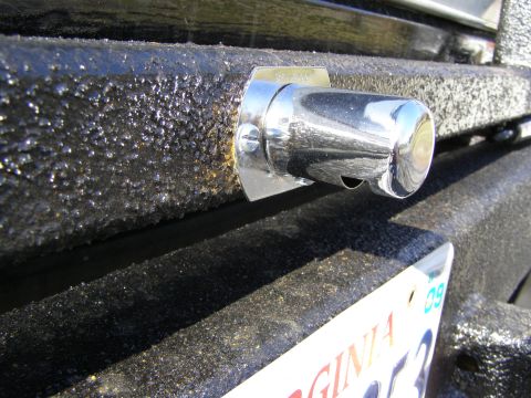 1993 Ford Bronco - A close-up view of a chrome reflector attached to a textured black bumper, with a partial license plate visible.