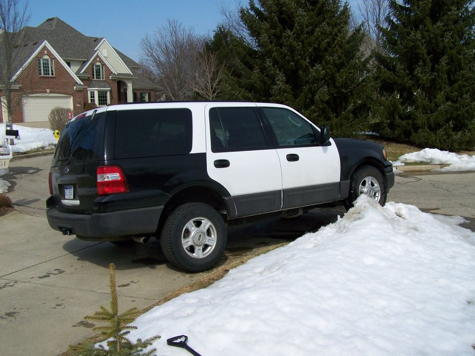 Black and white two-tone Ford Expedition SUV parked on a snowy suburban street, seen from the rear quarter