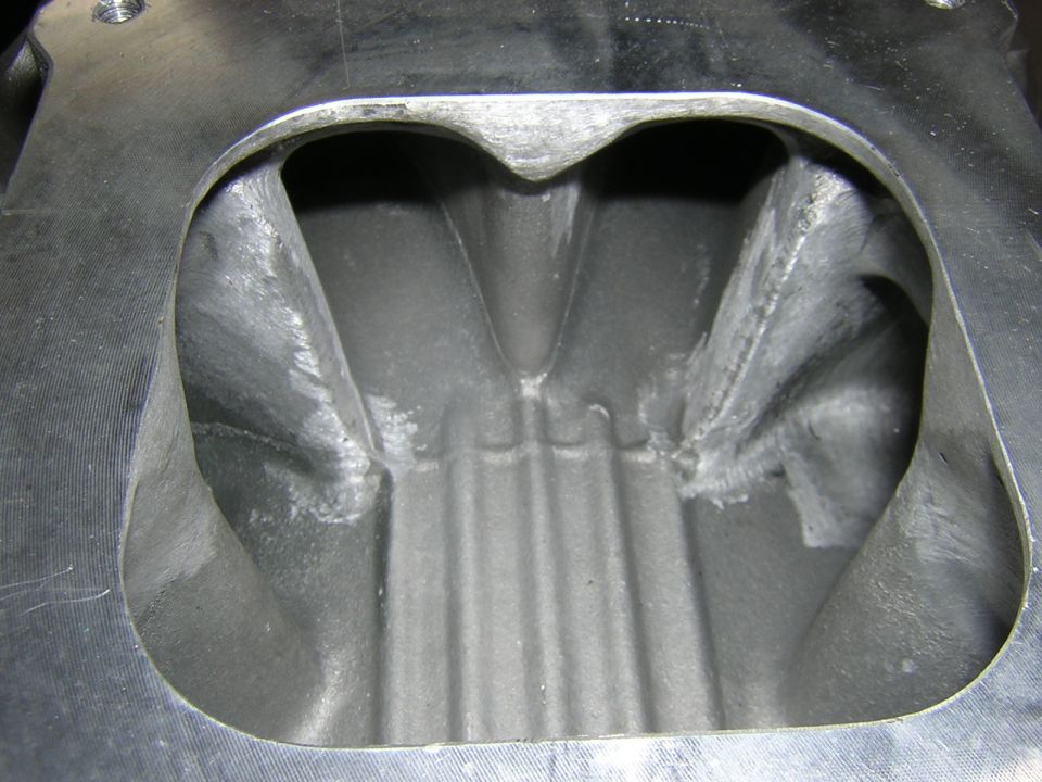 Down-view into an aluminum intake manifold carb flange showing ported plenum and runners