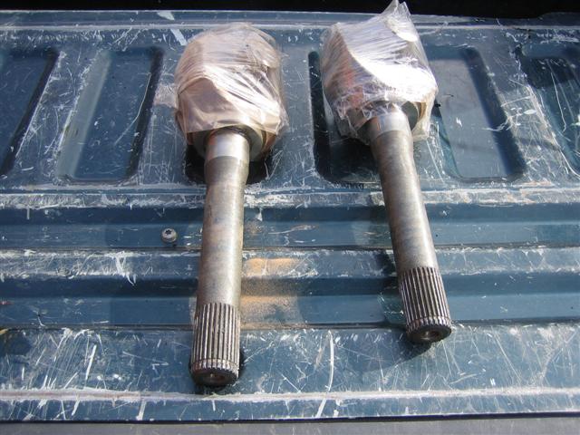Two drive shafts wrapped in plastic, resting on a dark blue truck bed