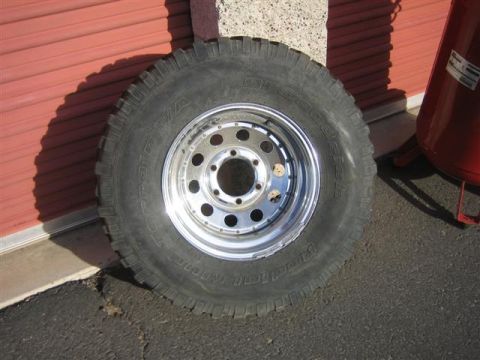 1994 Ford Bronco - A single tire and rim is shown leaning against a red corrugated wall, with a red air compressor visible to the right.