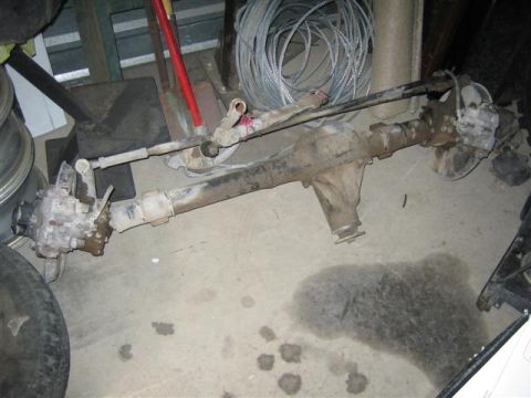 1994 Ford Bronco - Front axle assembly with steering linkage and brake components is shown on the floor.