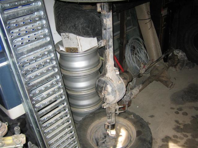 Stack of silver rims and vehicle axles in a cluttered garage
