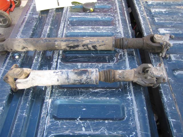 Two driveshafts, one black and one white, lying on a blue truck bed
