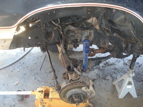 1989 Ford Bronco II - The front suspension and undercarriage of a vehicle are visible, supported by a yellow jack and jack stands.