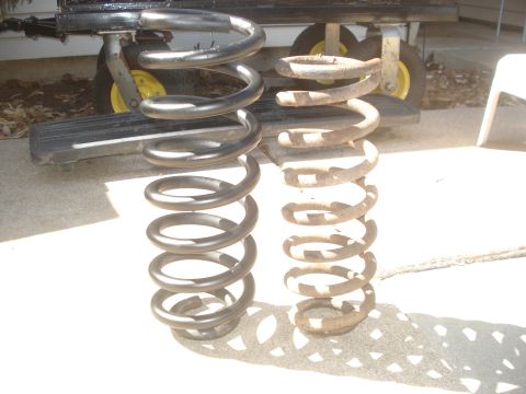 1989 Ford Bronco II - A new black coil spring is compared to an old rusty one, with a trailer visible behind them.