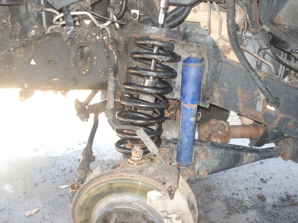 close-up of a vehicle's front suspension with coil spring and blue shock absorber
