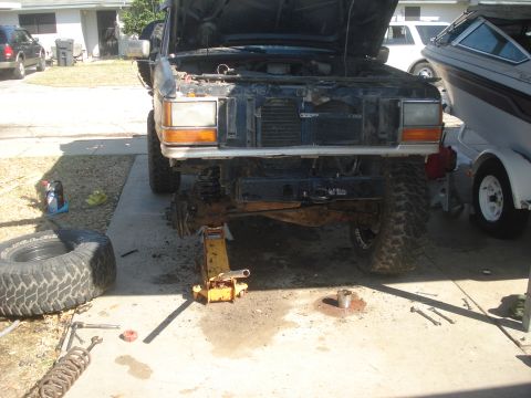 1989 Ford Bronco II - The front end of a 1989 Ford Bronco II is shown disassembled while on jack stands, with parts scattered around.