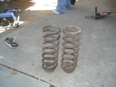 1989 Ford Bronco II - Two rusty coil springs are laid out on a concrete surface next to tools and a creeper.