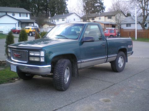1985 Ford Bronco II - A green GMC pickup truck is parked on a paved surface in front of houses.