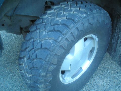 1985 Ford Bronco II - A close-up view of a vehicle's tire and wheel assembly, showing off-road tread and a silver rim.