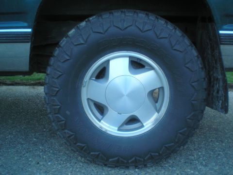 1985 Ford Bronco II - A close-up view of a vehicle's wheel and tire, a silver five-spoke rim and a knobby tread pattern.