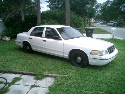 1999 Ford Crown Victoria - This white Ford Crown Victoria sedan is parked on a grassy lawn with trees and houses in the background.