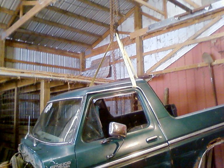Green 1978 Ford Bronco being lifted by chains inside a barn