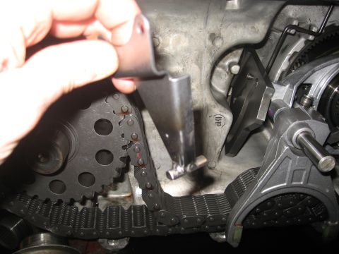1990 Ford F-250 - Close-up view of engine timing chain and gears with a hand holding a metal bracket.