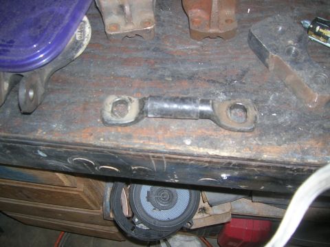 1985 Ford Bronco - A close-up view of a metal linkage part with a rubber boot, resting on a workbench.