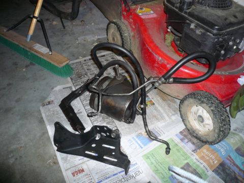 1975 Ford Ranchero - A brake booster assembly with associated lines is laid out on newspaper, with a red lawnmower and broom visible in the background.