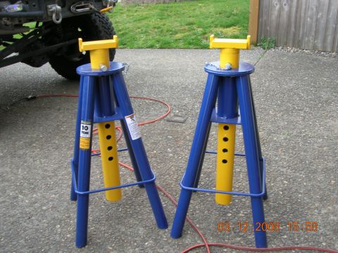 2008 Ford F-450 - Two heavy-duty jack stands are positioned on a paved surface, with a portion of a vehicle visible in the background.