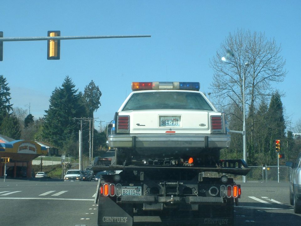 1987 Ford Crown Victoria LTD police car on a tow truck, rear view. License plate 98J-VJT