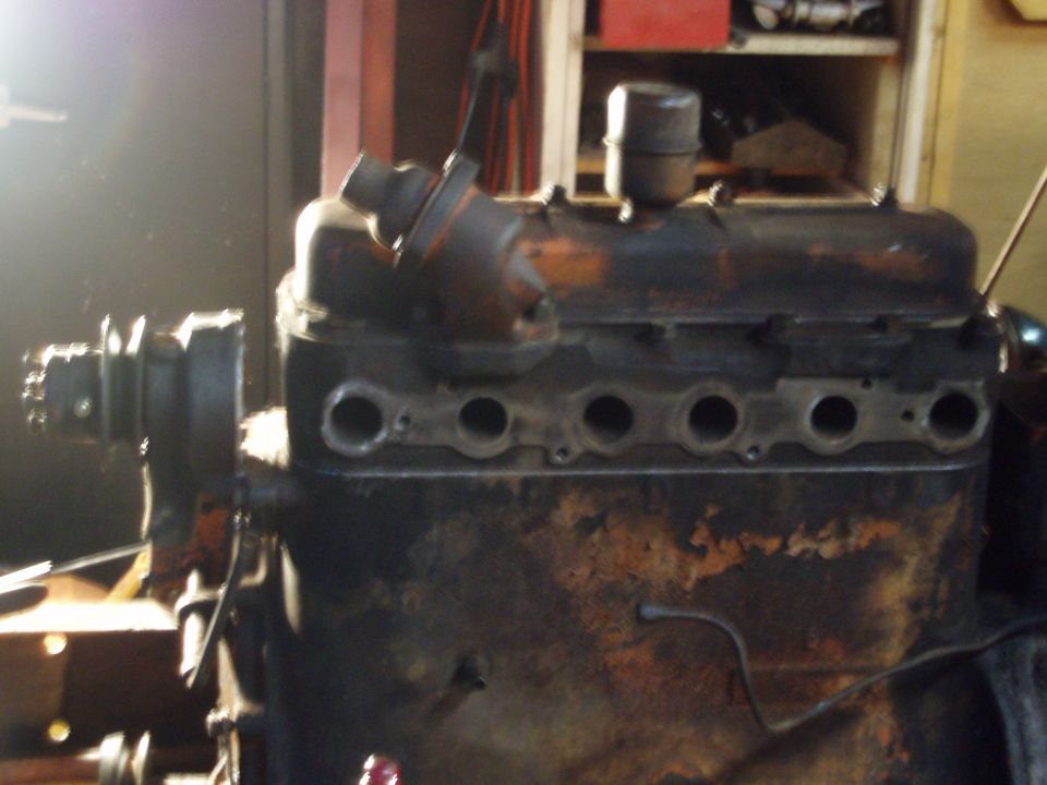 Rusty inline-six engine on a stand in a garage, manifolds removed exposing head ports