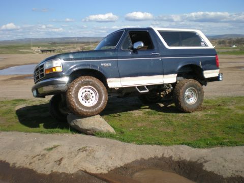 1993 Ford Bronco - 1993 Ford Bronco with a lifted suspension and off-road tires navigates rocky terrain.