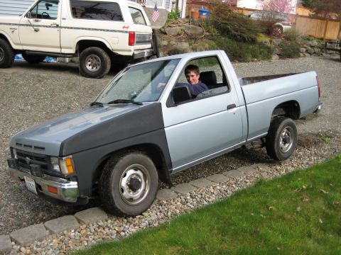 1980 Ford Bronco - A silver pickup truck with a black hood is parked on a gravel driveway, with another vehicle in the background.