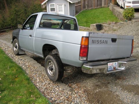 1980 Ford Bronco - This Nissan pickup truck is parked on a gravel driveway next to a grassy area and a small building.