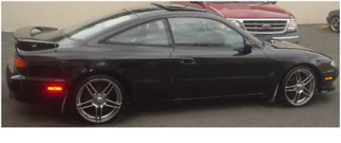 1993 Mazda MX-6 - A black 1993 Mazda MX-6 is seen from the side, custom wheels and a rear spoiler.