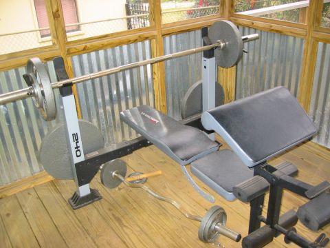 1996 Ford Bronco - A weight bench and barbells are set up on a wooden floor with a corrugated metal wall in the background.