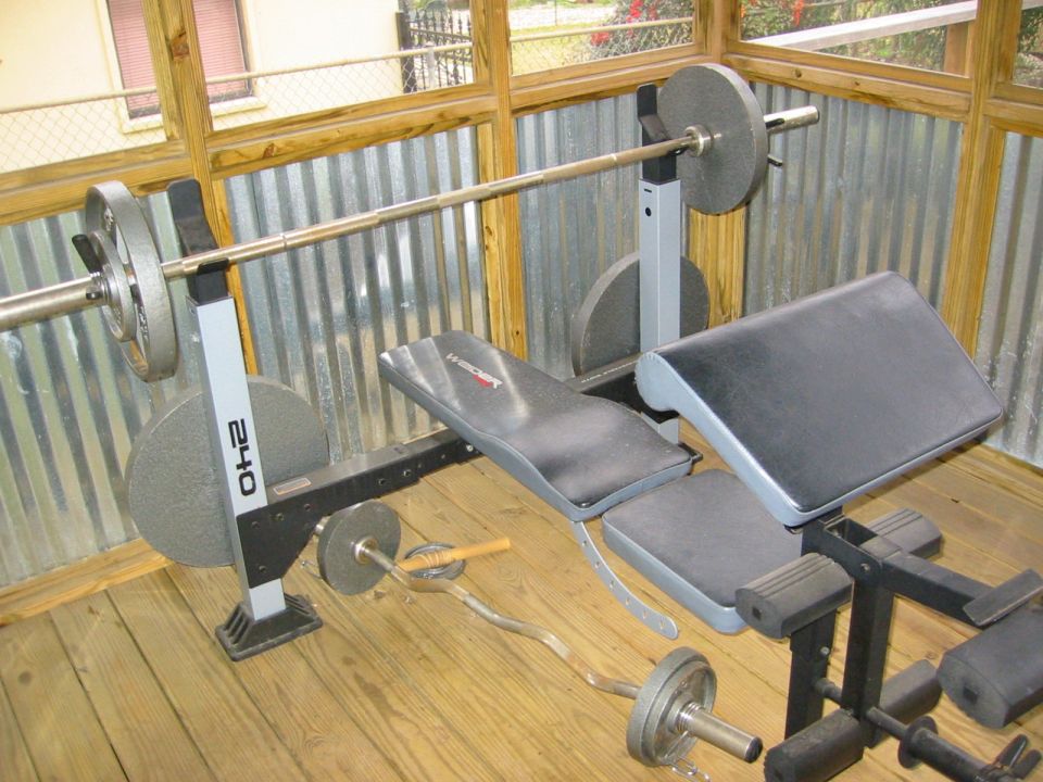 Weight bench with barbells and weight plates on wooden floor, corrugated metal wall behind